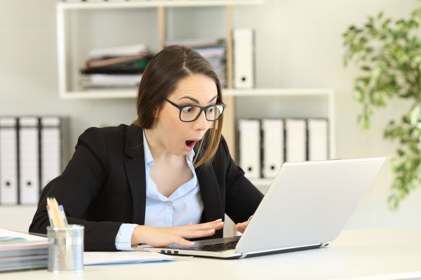 Amazed office worker reading good news in a computer on a desktop